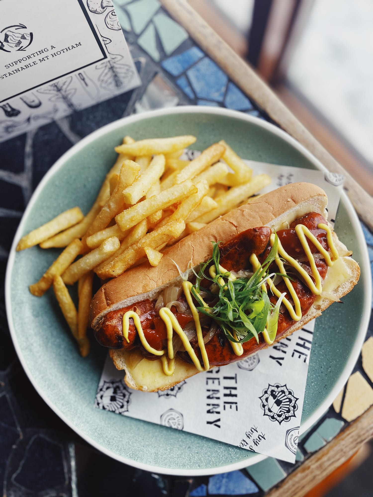 A loaded hot dog with a side of chips on a Genny plate