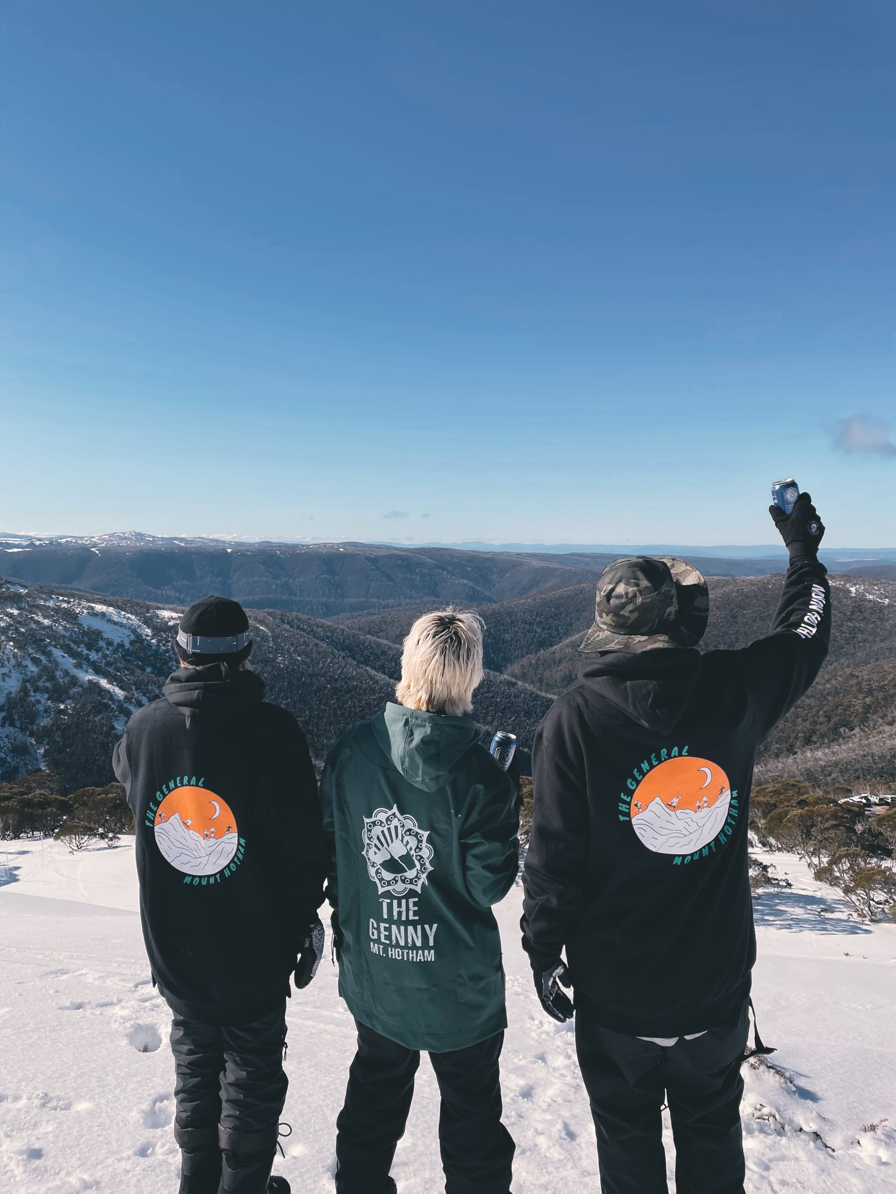 Three friends in The Genny snow gear standing in the snow looking out over the Bogong High Plains at Mt Hotham