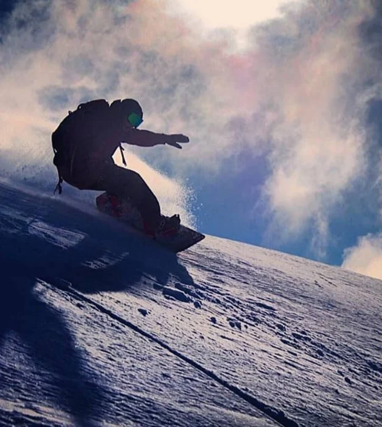 A snowboarder carving down a Mt Hotham slope, throwing a wall of spray
